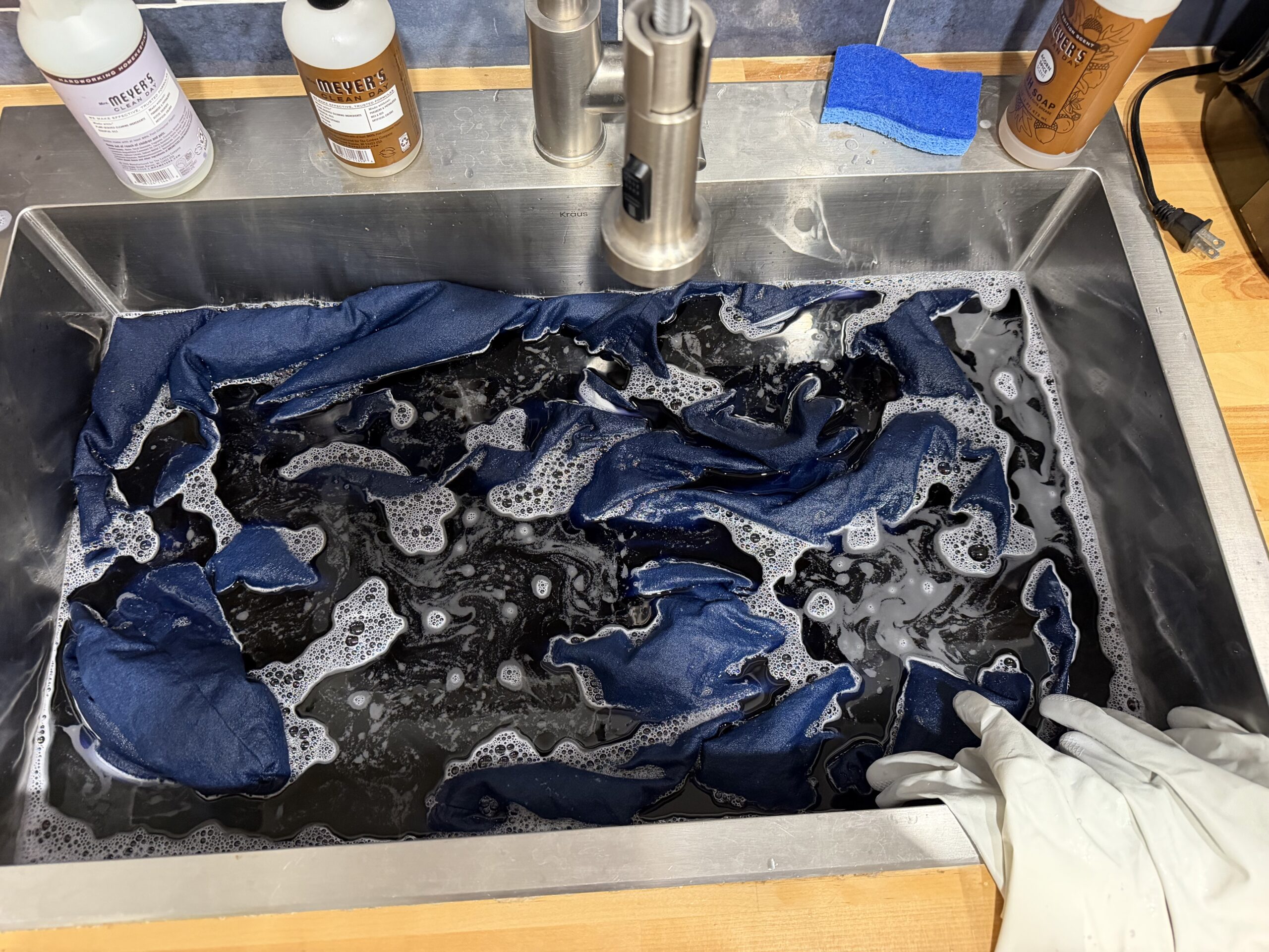 Blue denim couch slipcovers soaking in Rit dye in a stainless steel kitchen sink